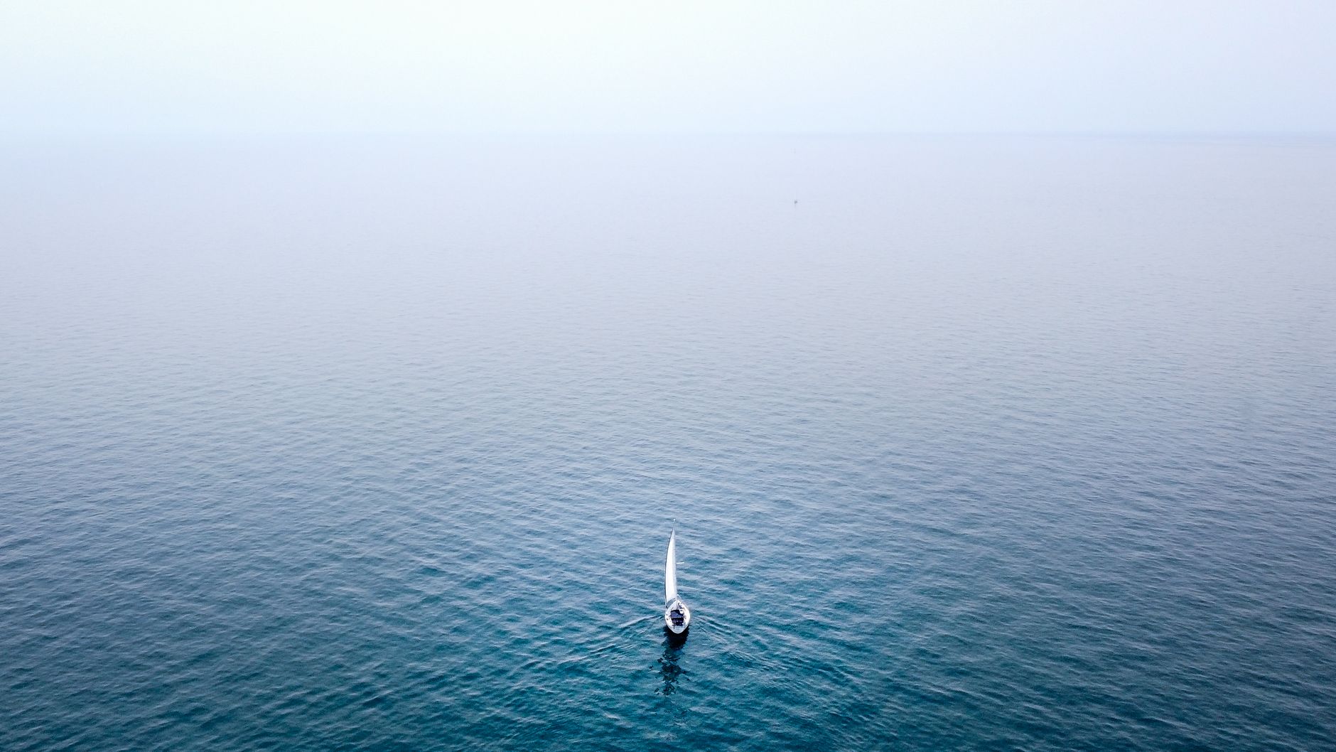 A lone sailboat sails on the serene waters of Lake Michigan under a clear sky.