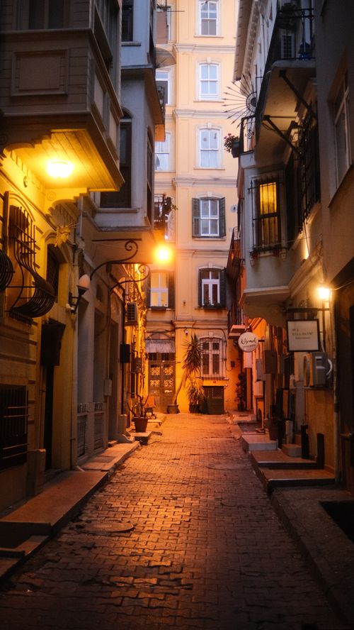 Free A quaint cobblestone alleyway in a European city illuminated by warm streetlights at twilight. Stock Photo