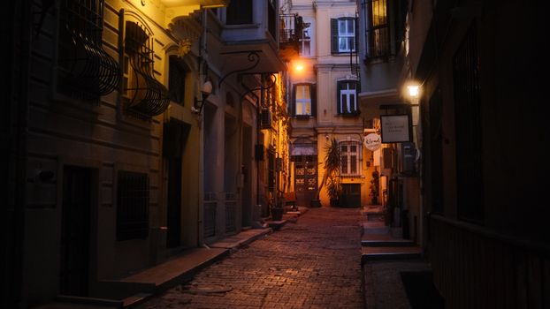A narrow, cobblestone street illuminated by warm lights in a historic European city at night.