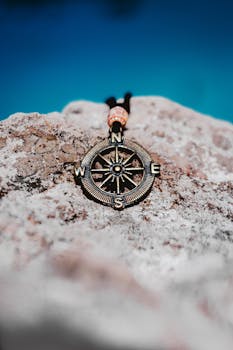 From above of stylish metal pendant in shape of compass placed on white rock