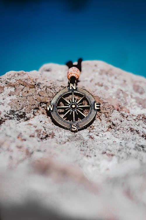 From above of stylish metal pendant in shape of compass placed on white rock