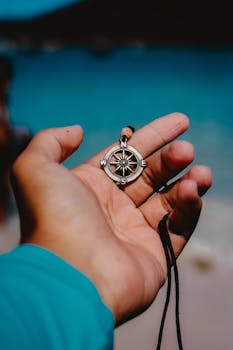 一只手拿着指南针吊坠，背景是模糊的海滩