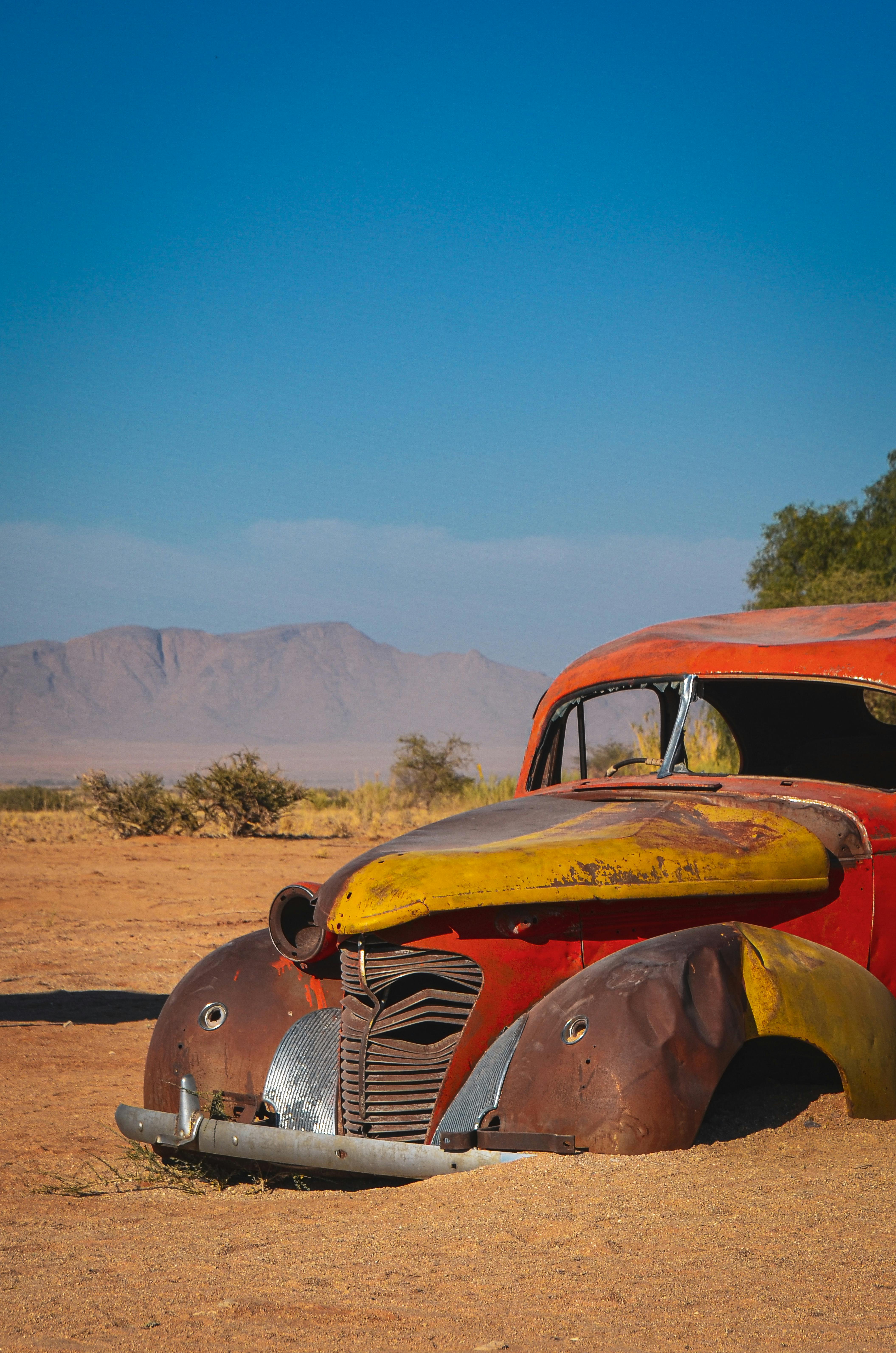 A vintage car rusting in a desert setting with mountains in the background.