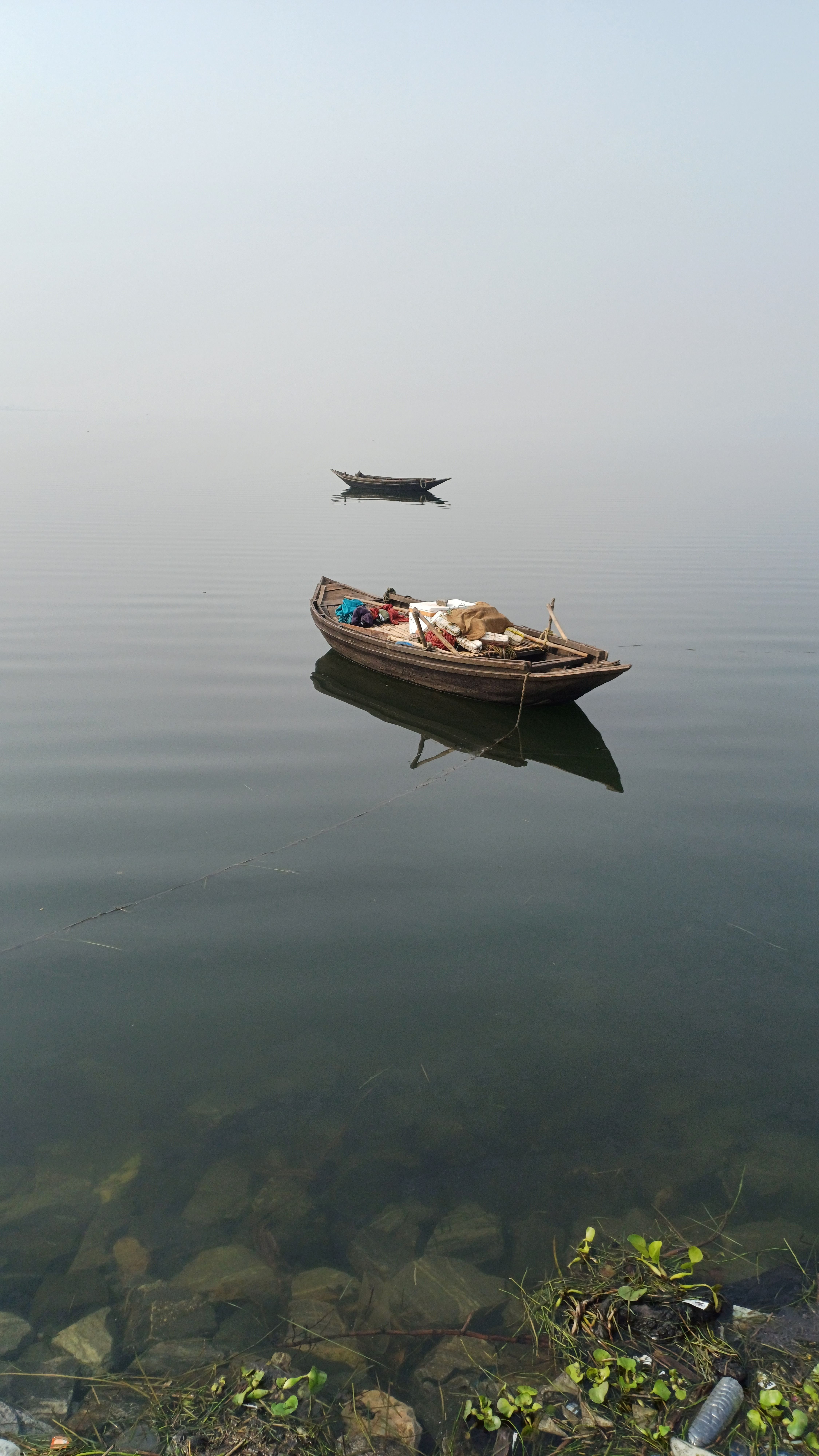 Two wooden boats float on a serene, foggy lake creating a peaceful scene.