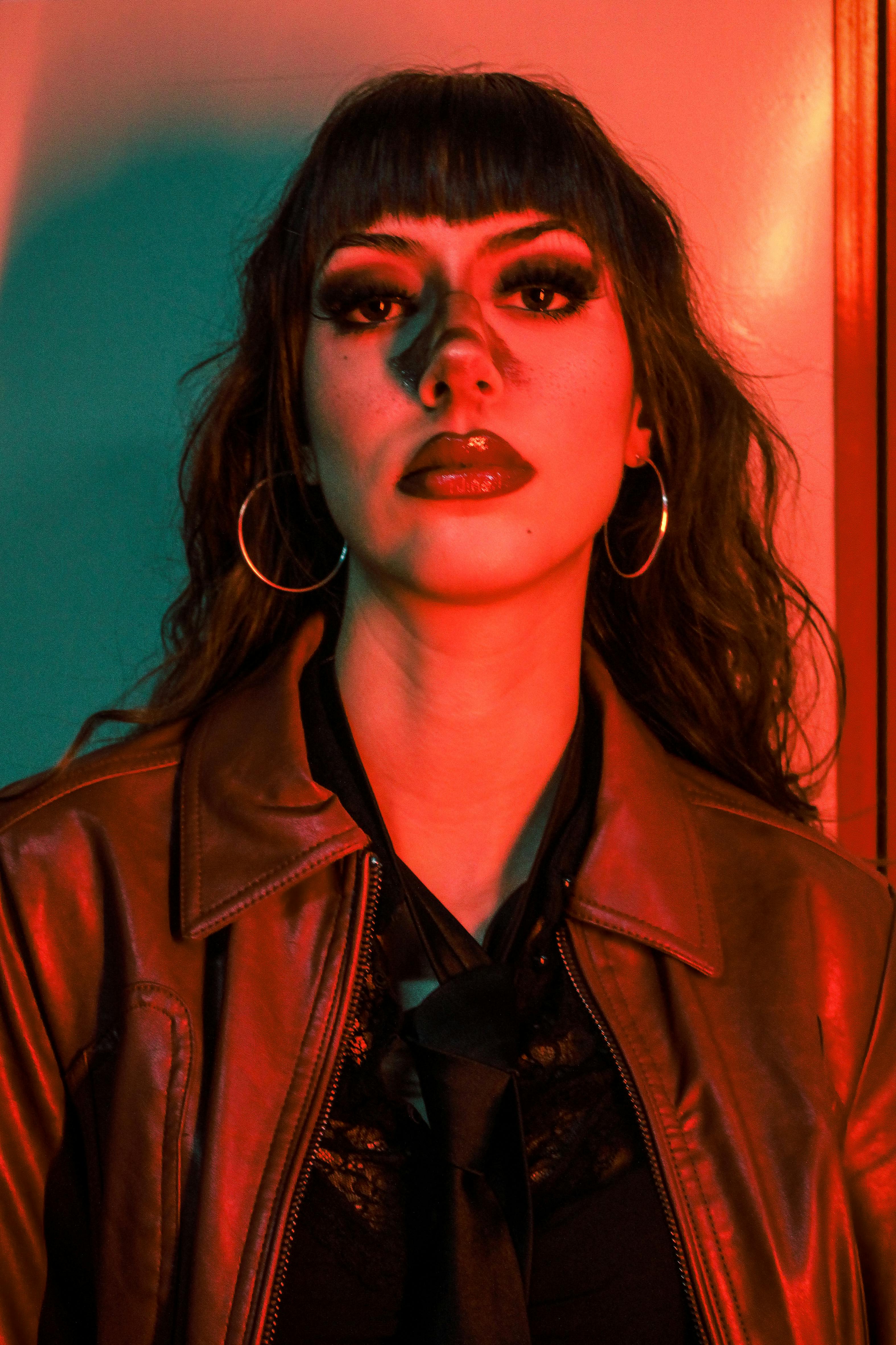 A striking portrait of a woman with bold makeup, highlighted by dramatic red and green lighting.