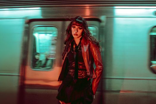 A stylish woman stands confidently in a subway station, vibrant lighting enhancing the urban scene.