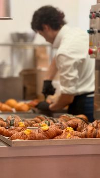 A chef in a bakery kitchen preparing trays of freshly baked croissants with attention to detail.