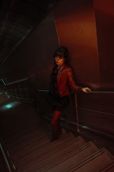 Dramatic portrait of a woman standing on a dimly lit metal staircase at night.