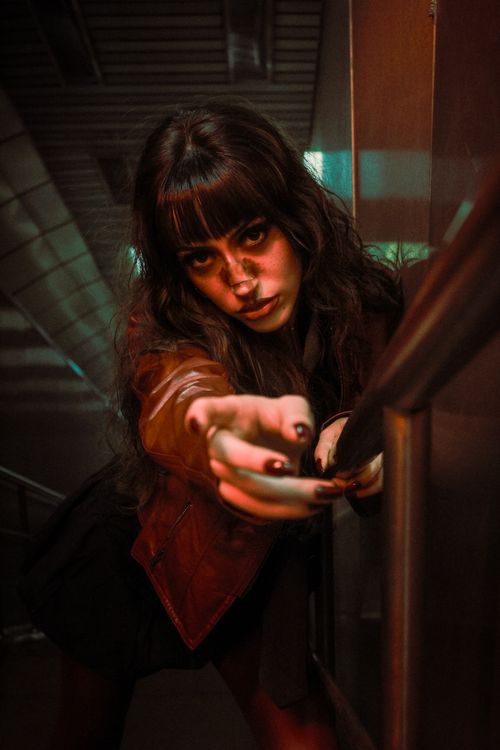 Free Dramatic portrait of a woman with intense gaze reaching out in dim urban lighting. Stock Photo