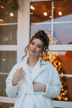 Elegant woman in white coat enjoying winter outdoors by festive lights.