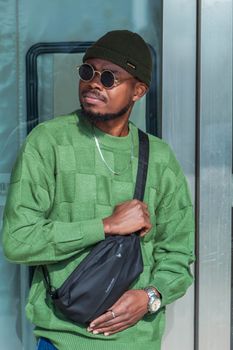 A fashionable man in a green sweater with sunglasses outdoors on a sunny day.