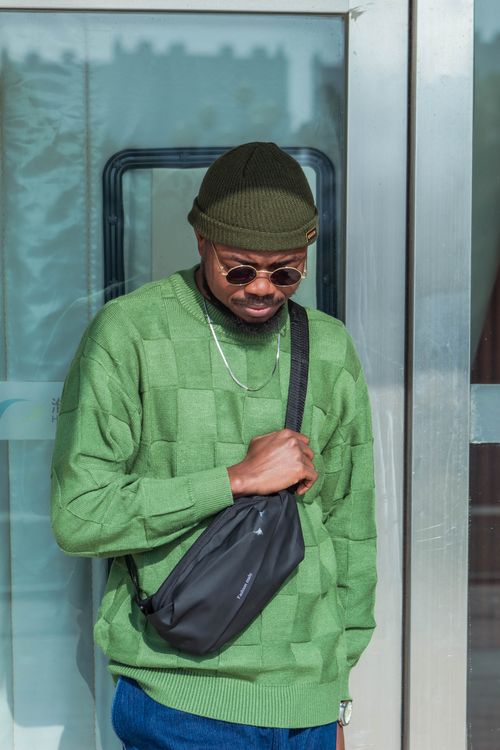 Free Stylish man in sunglasses and green sweater with a bag stands in front of a glass door outdoors. Stock Photo