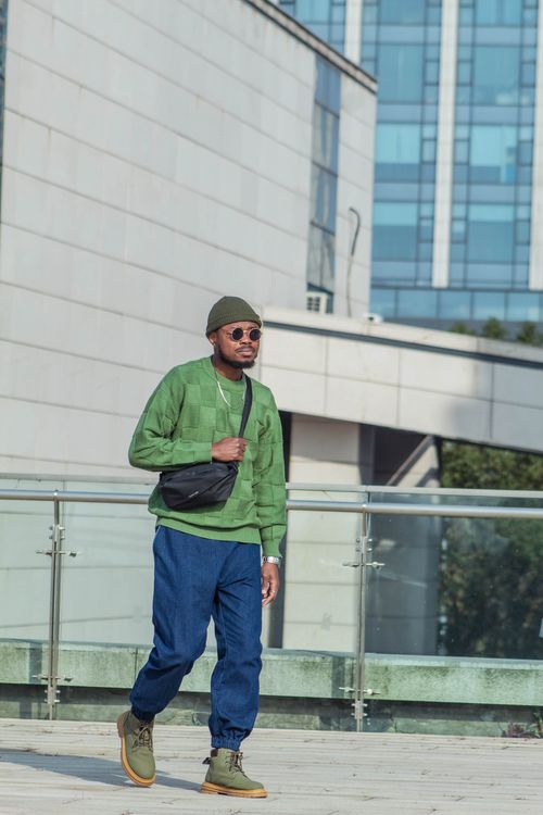 Free Stylish man wearing green sweater and blue pants walking in urban cityscape. Stock Photo