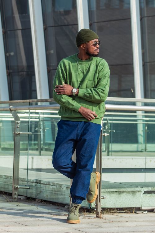 Free Fashionable man in green sweater and blue jeans standing outside near modern glass building. Stock Photo