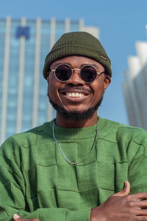 Free Man smiling outdoors in a green sweater and sunglasses against urban backdrop Stock Photo