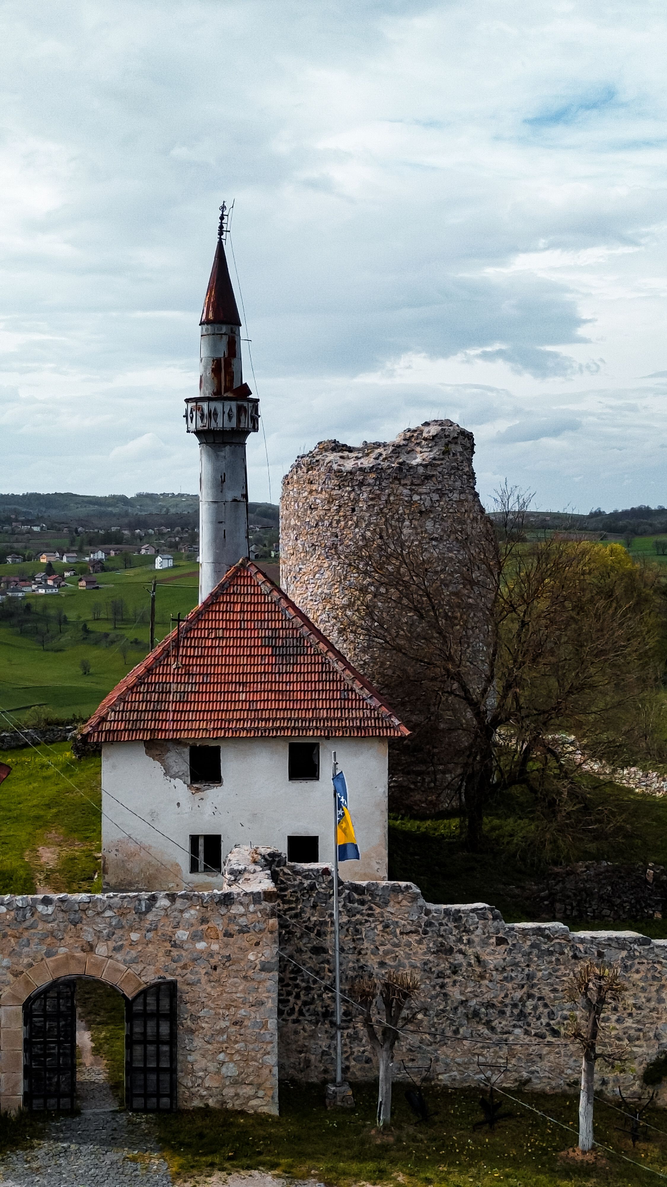 A scenic view of a historic fortress with a minaret and a flag in a countryside setting.