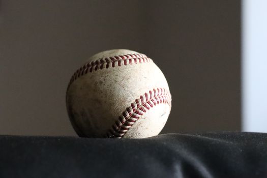 High-resolution image of a worn baseball on a dark surface, highlighting its stitching and texture.