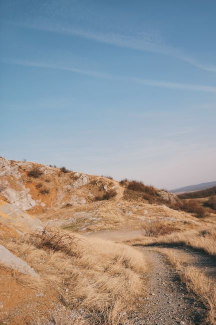 A winding dirt path cuts through a dry, barren landscape under a clear blue sky.