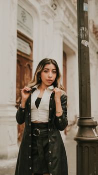 Young woman in fashionable outfit posing confidently in a historic urban street setting.