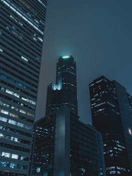 Moody nighttime cityscape featuring towering skyscrapers illuminated by soft lights.