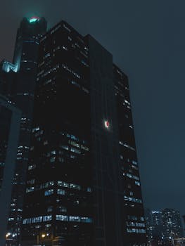 Dramatic night view of tall skyscrapers in a city with glowing lights.