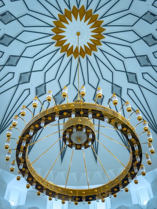 Free A stunning golden chandelier hanging beneath a geometric patterned dome ceiling in a mosque. Stock Photo