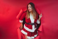 A woman dressed as Santa Claus playfully tearing through a red backdrop, exuding holiday cheer.