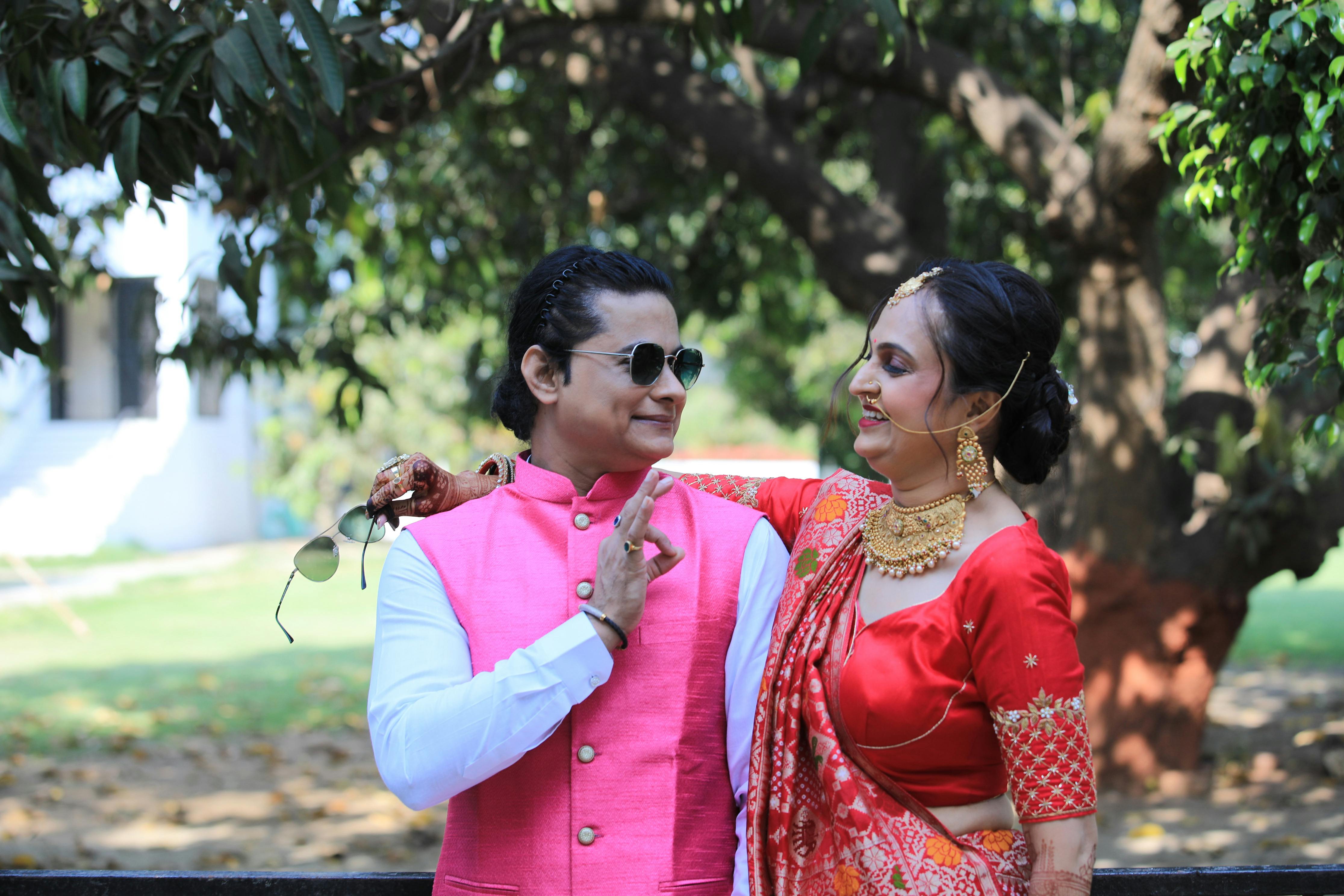 A stylish couple poses outdoors in traditional Indian attire, showcasing vibrant colors and chic jewelry.