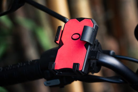 Close-up of a red phone holder mounted on a bicycle handlebar outdoors.