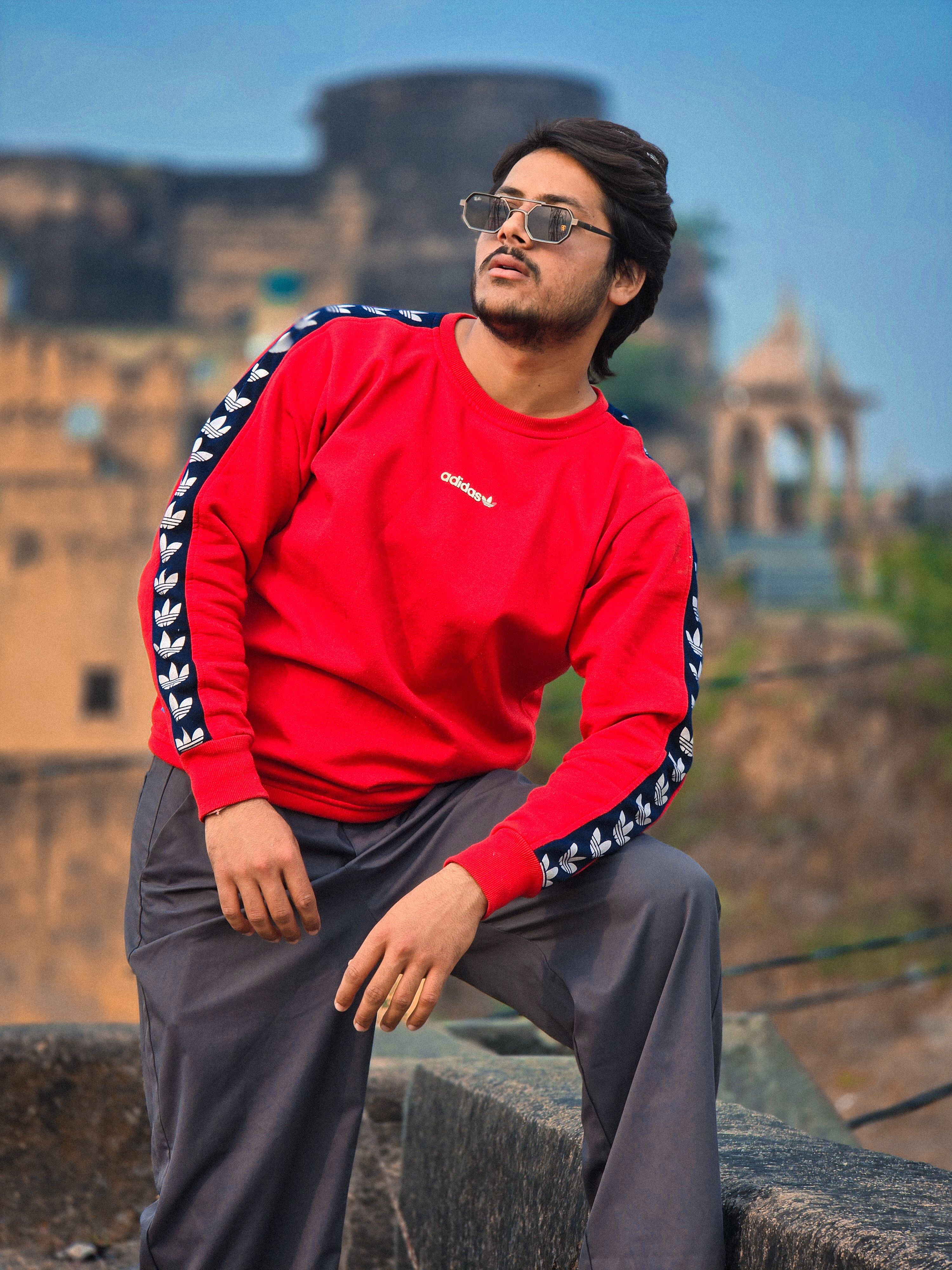 Stylish young man in red sweater poses at a historic landmark, exuding confidence and modern fashion.