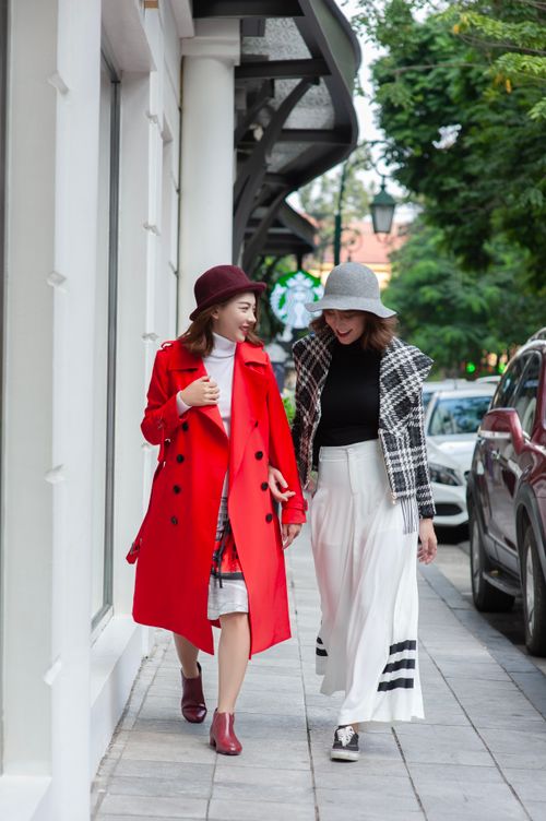 Free Two fashionable women walking on a city sidewalk, dressed in stylish coats and hats. Stock Photo