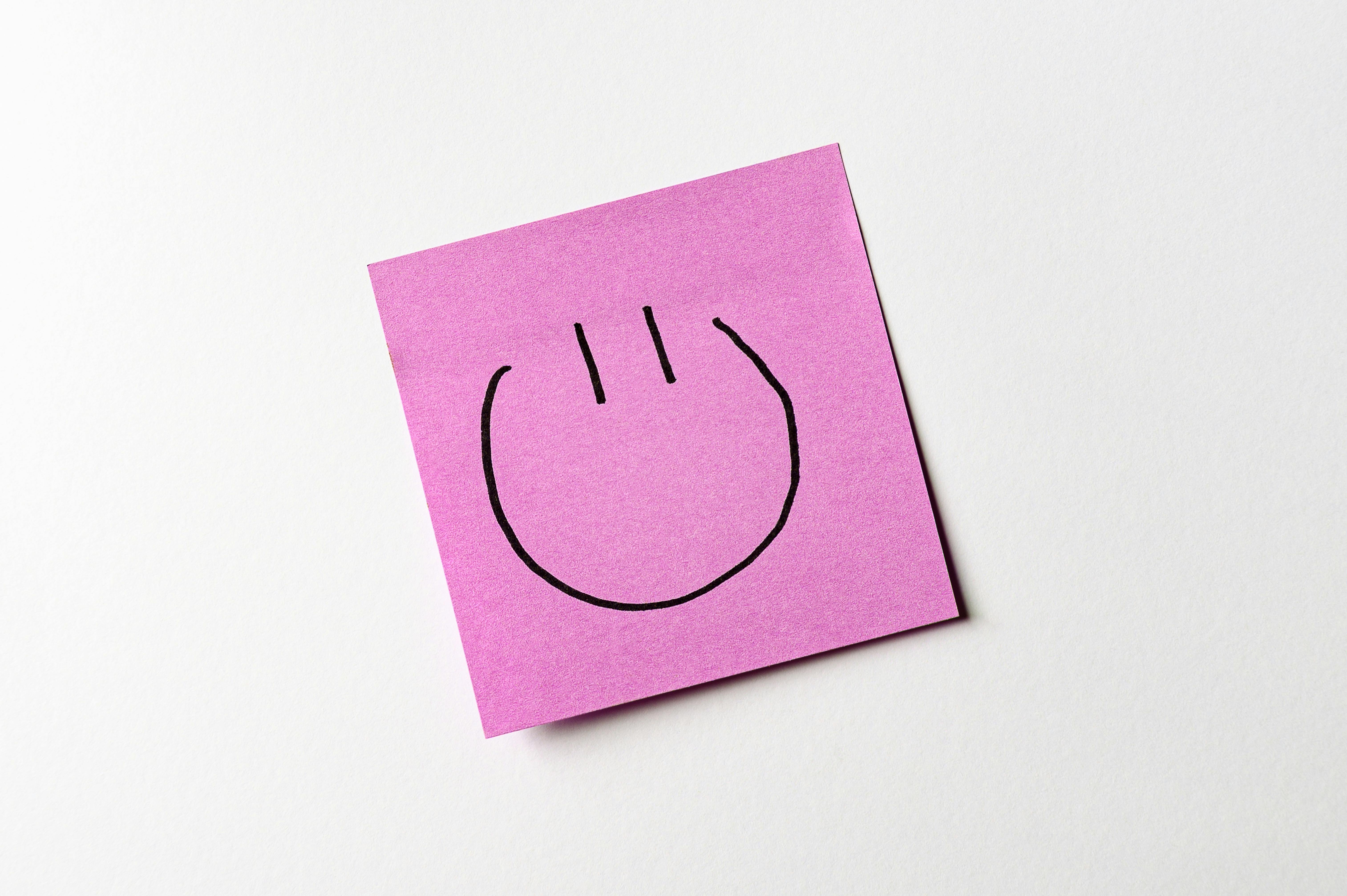 Kostenlos Ein einfaches Smiley-Gesicht, gezeichnet auf einen rosa Haftzettel vor weißem Hintergrund. Stock-Foto