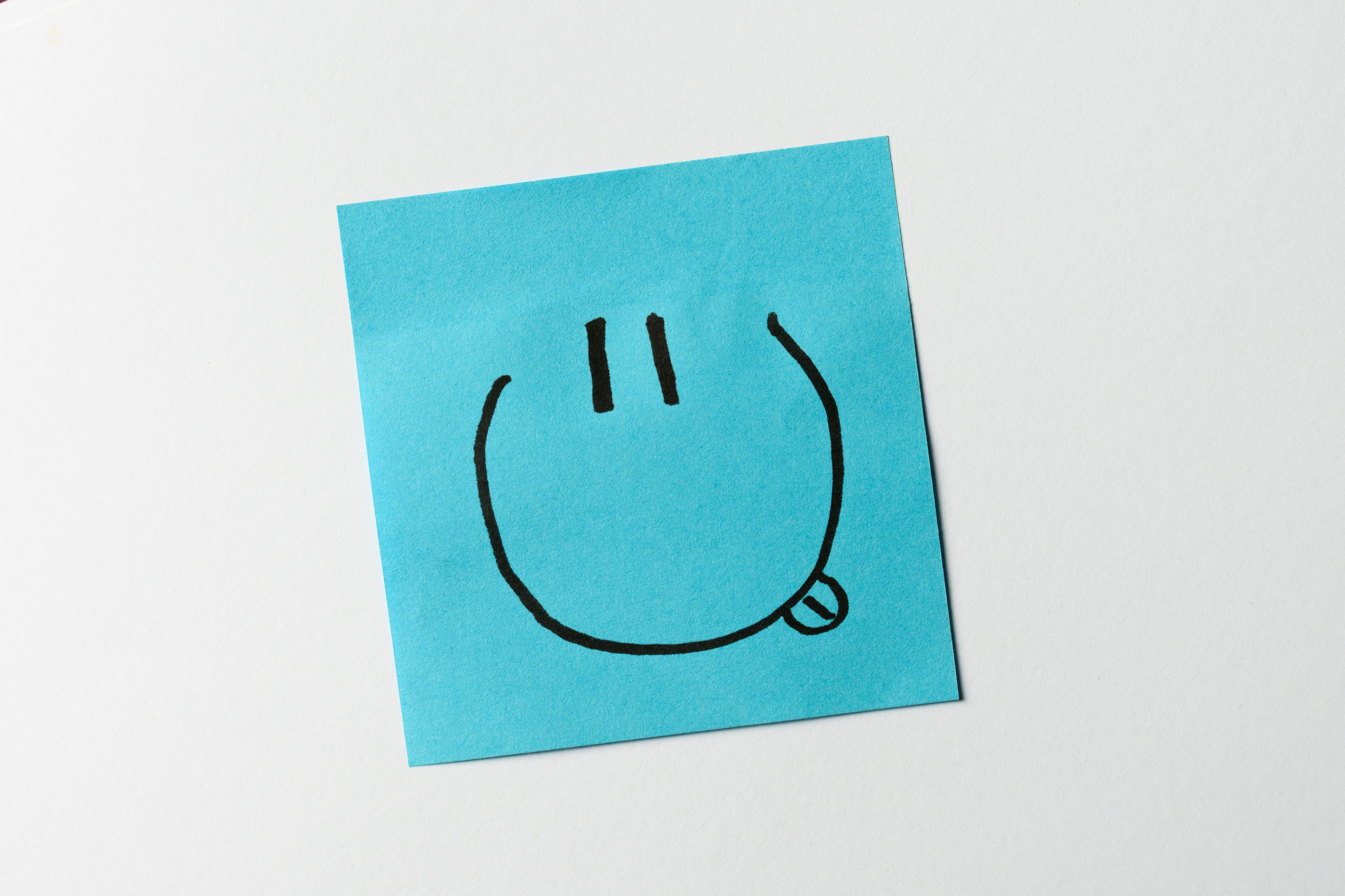 Gratis Una nota adhesiva de color azul que presenta una cara sonriente sencilla dibujada a mano con una expresión de lengua afuera. Foto de stock