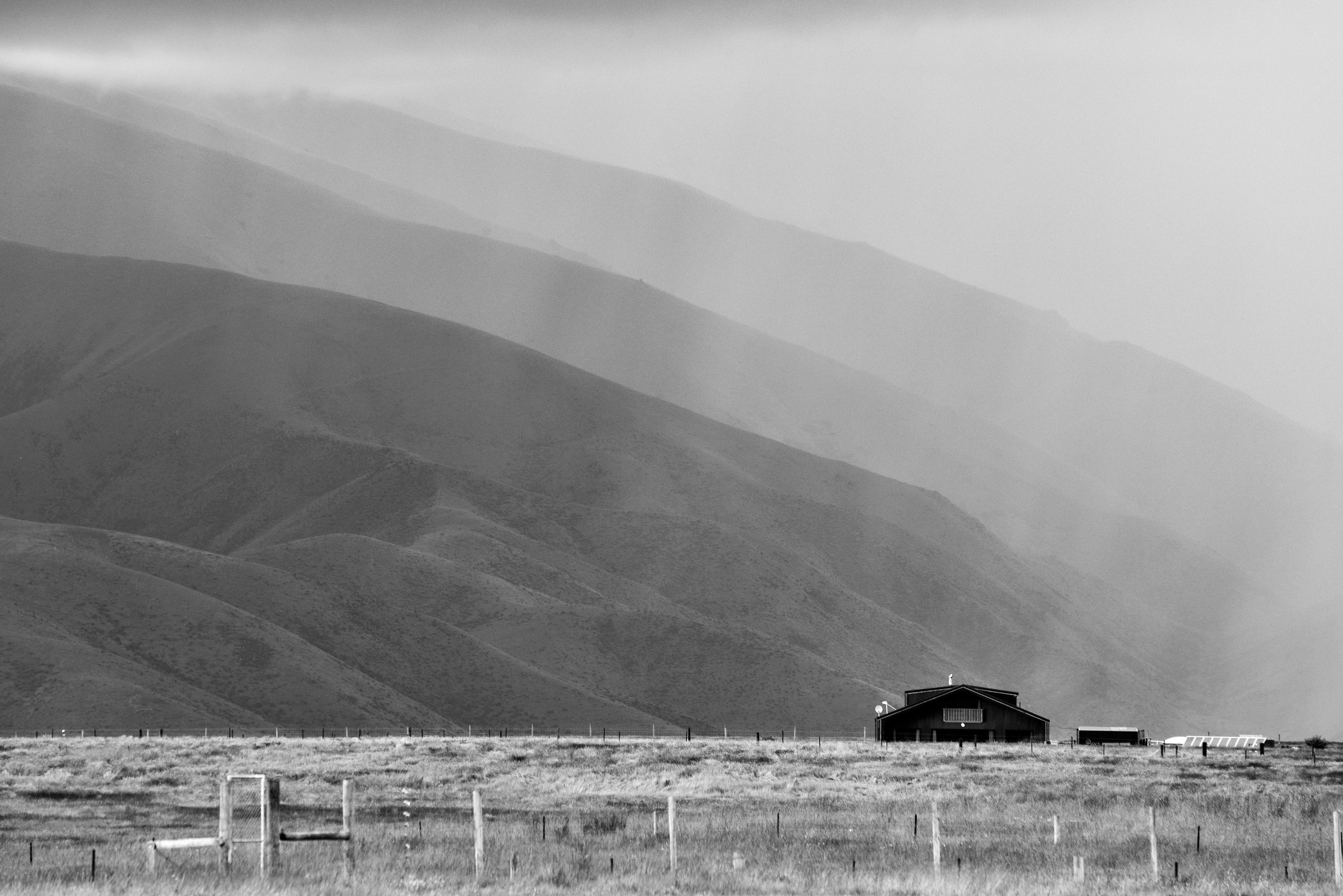 A tranquil wooden cabin nestled among misty mountains, captured in monochrome.