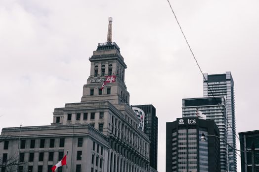 View of the Canada Life Building in Toronto with surrounding skyscrapers on a cloudy day.