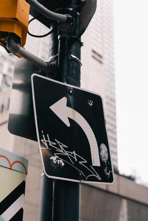 Free A street sign with graffiti and a skyscraper in the background, captured in an urban environment. Stock Photo
