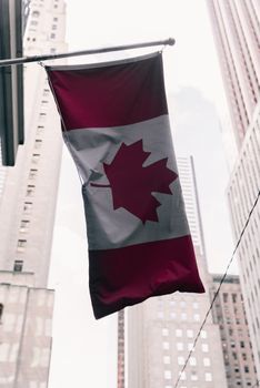 The Canadian flag waves against a backdrop of city skyscrapers, symbolizing national pride.