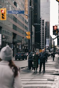 People crossing Yonge Street in Toronto with city skyscrapers in the background.