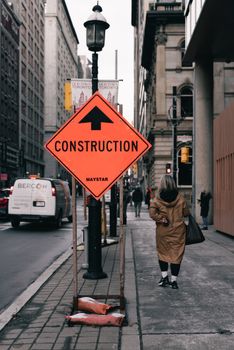 A city street with construction signs, buildings, and a pedestrian walking by. Urban development vibrant scene.