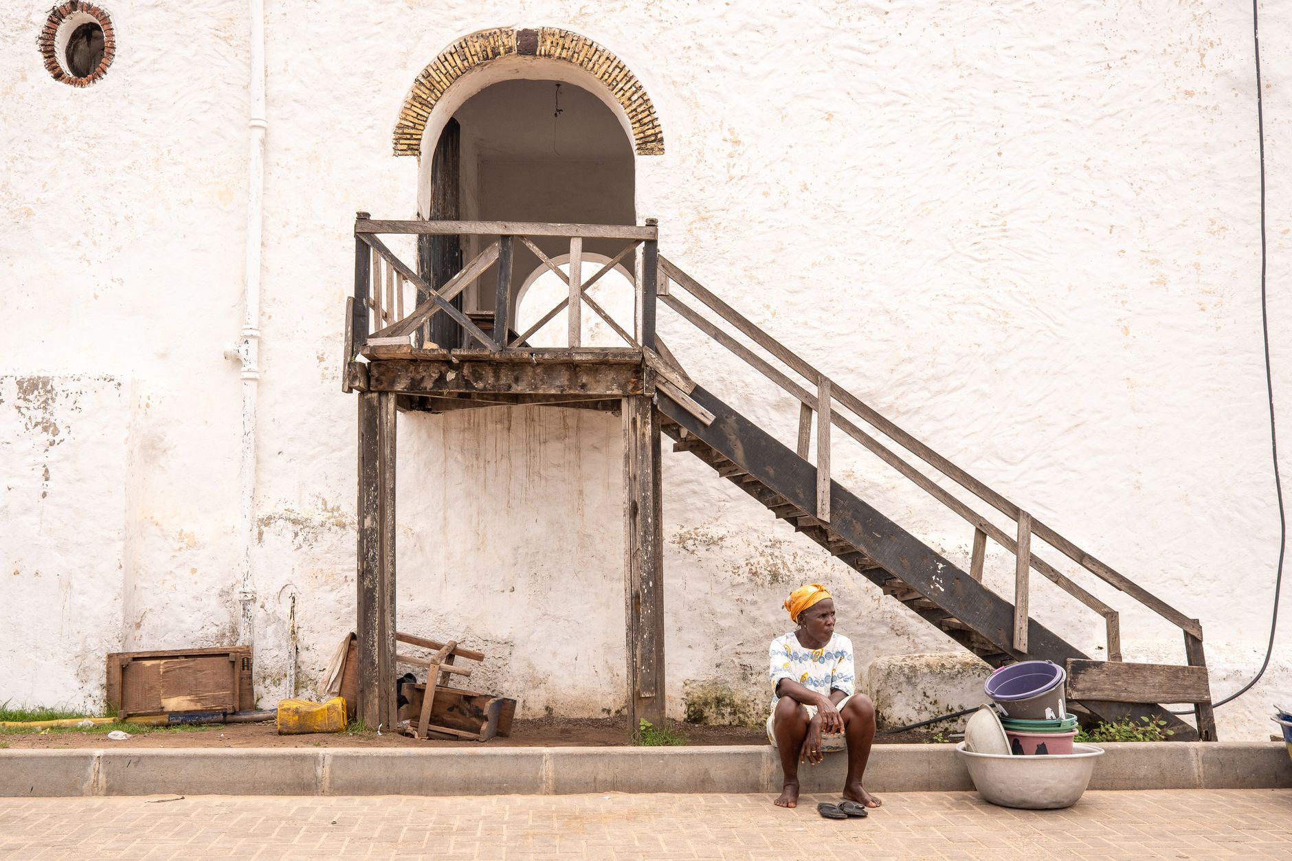 African woman resting by a historic structure in Elmina, Ghana. Captures local architecture.