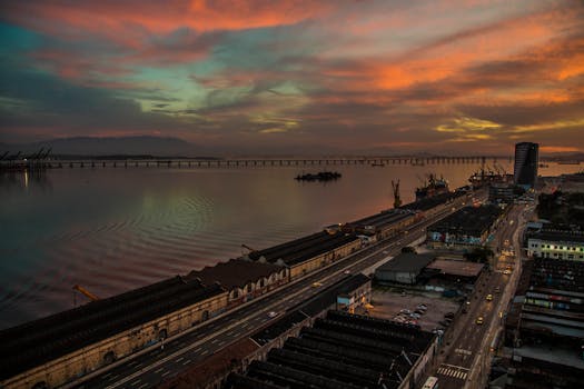 A breathtaking aerial view of Rio de Janeiro's waterfront at sunset, featuring vibrant skies and the iconic bridge.