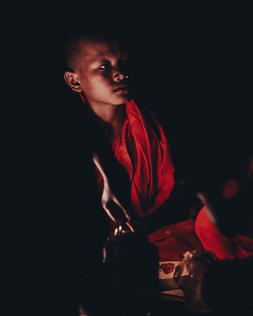 Free A young monk in traditional red robe illuminated by warm candlelight during a night gathering in Cambodia. Stock Photo