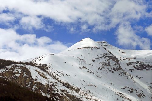 Free Stunning view of a snow-covered mountain peak against a vibrant blue sky with fluffy clouds. Stock Photo