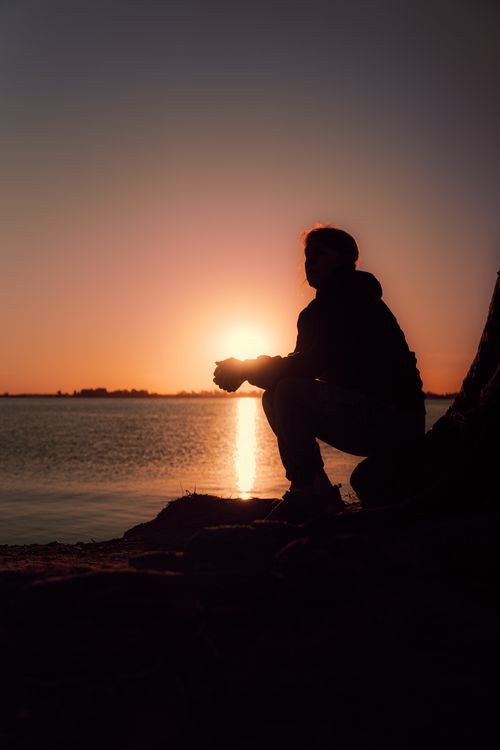 Free A silhouette of a person sitting by the sea during a vibrant sunset, capturing serene tranquility. Stock Photo
