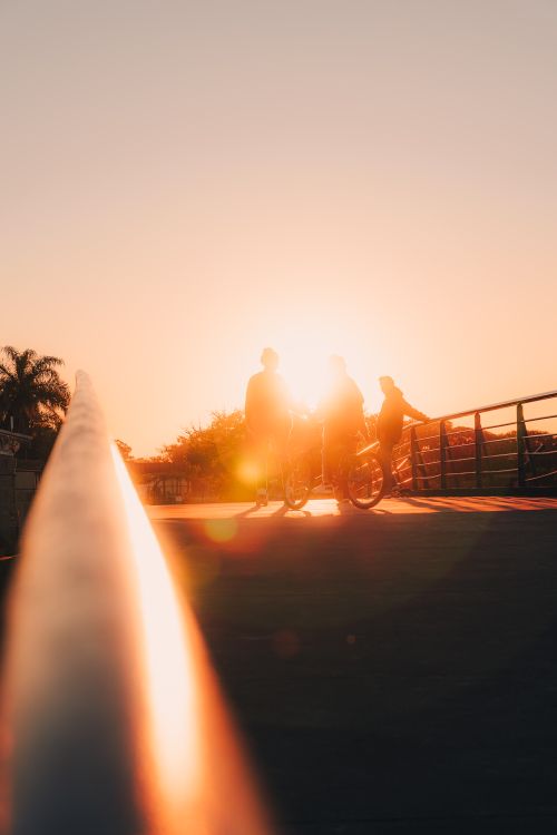 Free Silhouettes of cyclists on a bridge at sunset, creating a warm and peaceful scene. Stock Photo