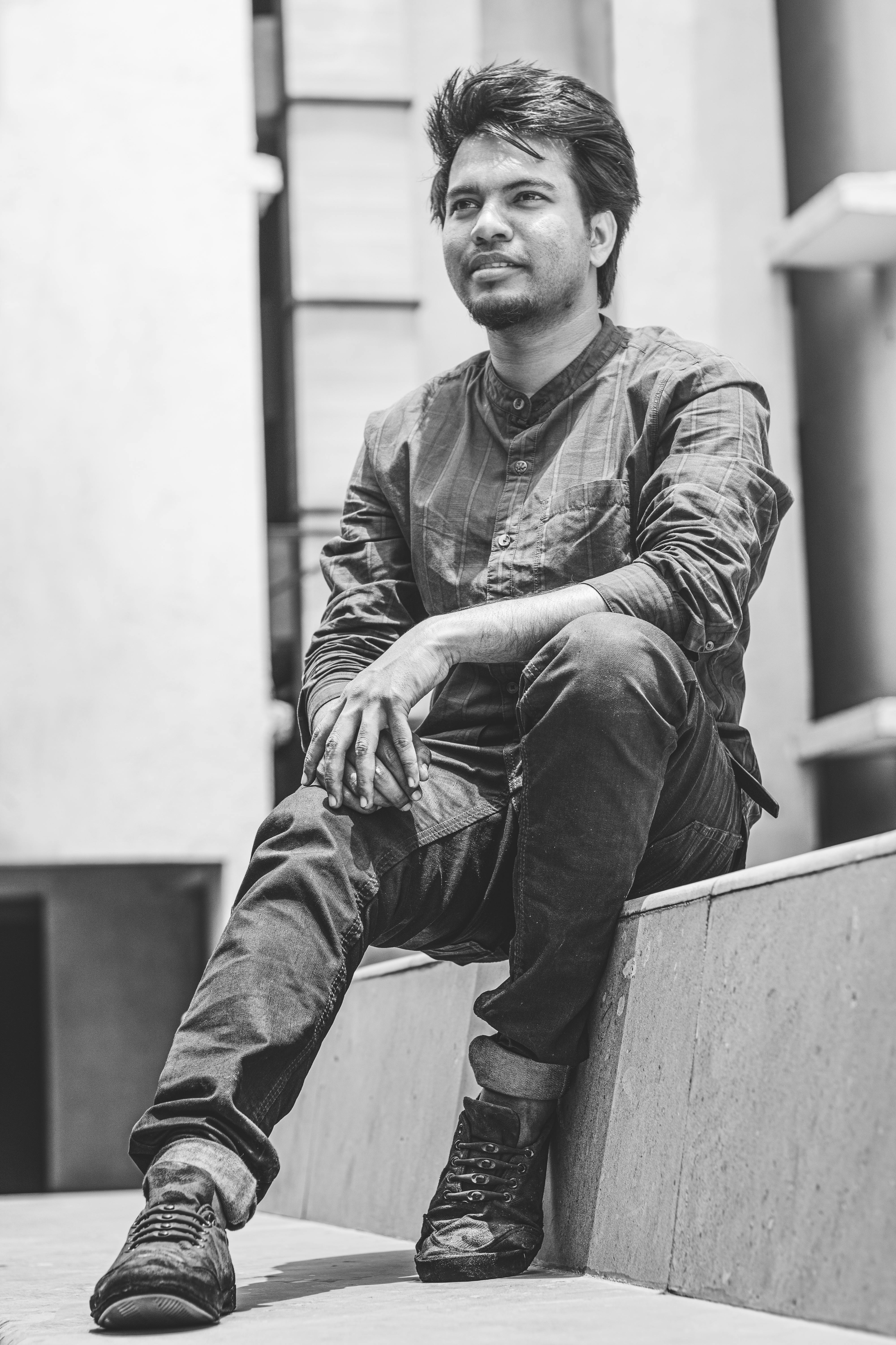 Free Black and white portrait of a stylish man sitting outdoors, capturing a relaxed and modern vibe. Stock Photo