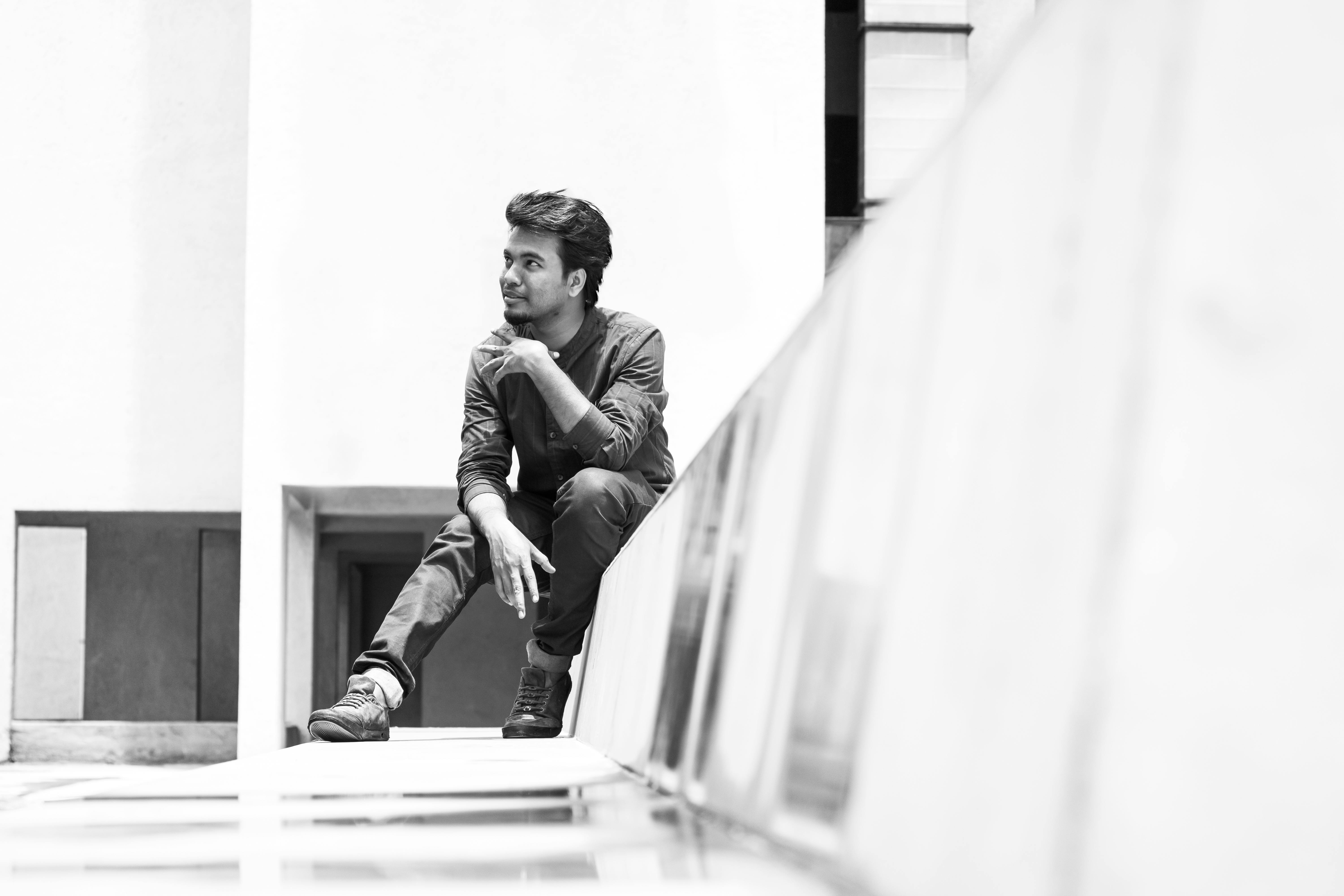 Free Elegant black and white portrait of a young man sitting outdoors, showcasing modern fashion. Stock Photo