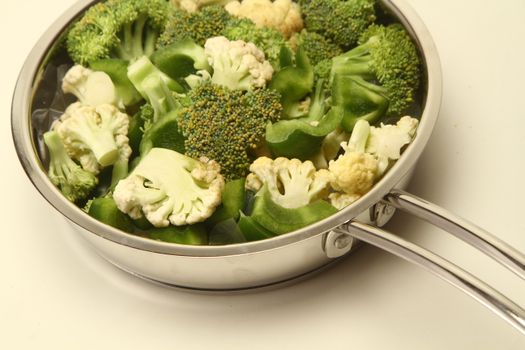 Sliced broccoli and cauliflower in a stainless steel pan on a light background.