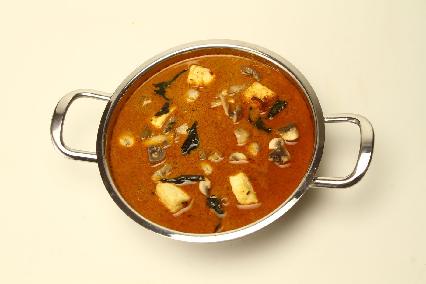A rich and vibrant paneer mushroom curry served in a stainless steel dish.