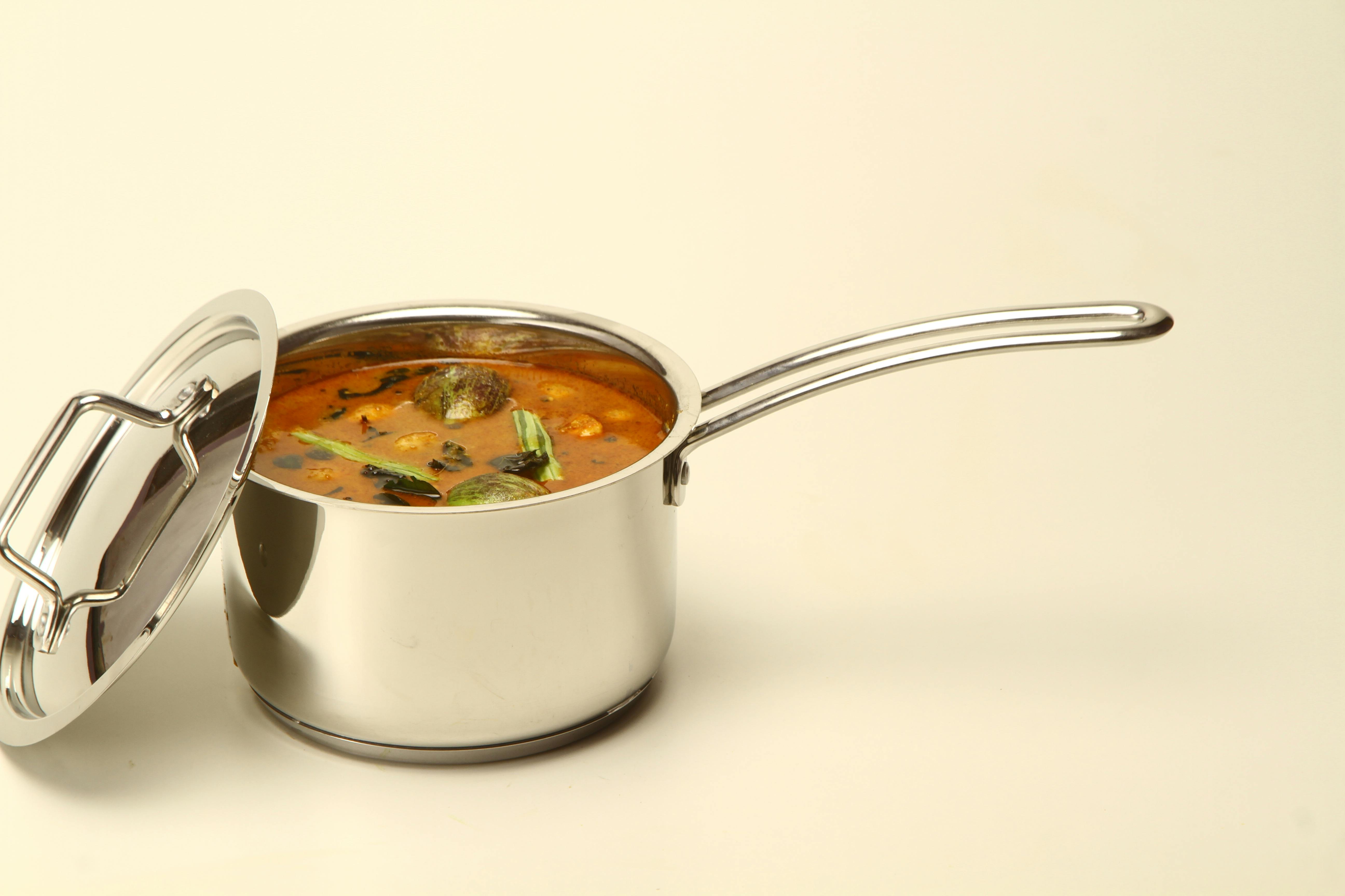 A stainless steel pot filled with flavorful Indian curry and vibrant curry leaves.